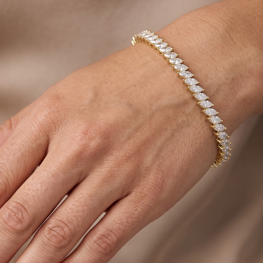 A close-up of a gold tennis bracelet with marquise-cut clear moissanite stones worn on a person's wrist.