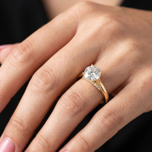 Gold ring with a moissanite diamond on a person's finger against a dark background