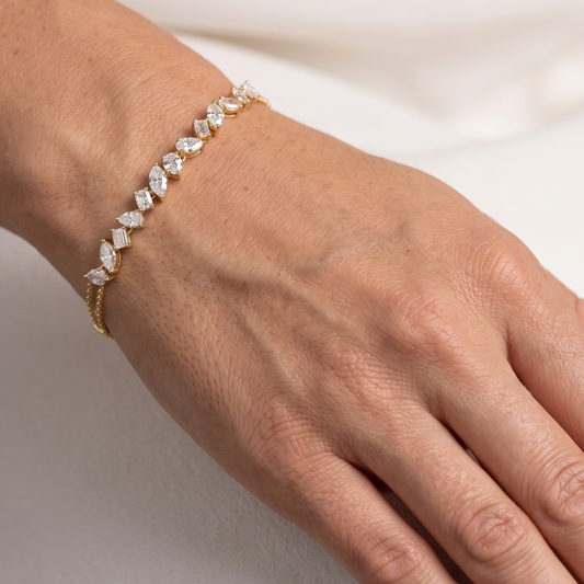 A delicate yellow gold bracelet with marquise and baguette-cut clear moissanite stones, shown worn on a person's wrist against a soft white background.
