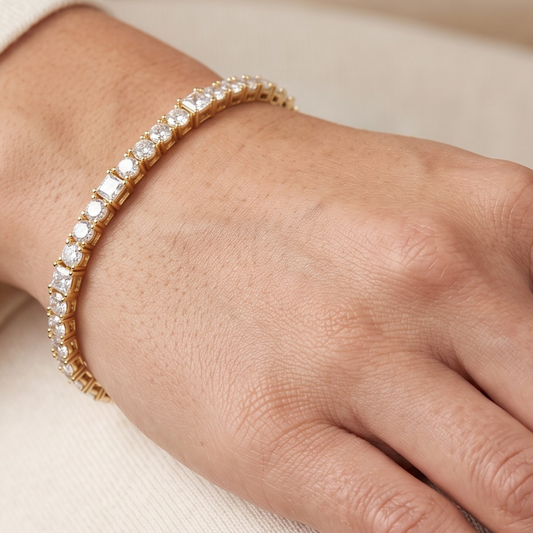 A close-up of a gold tennis bracelet with clear rectangular moissanite gemstones worn on a person's wrist.