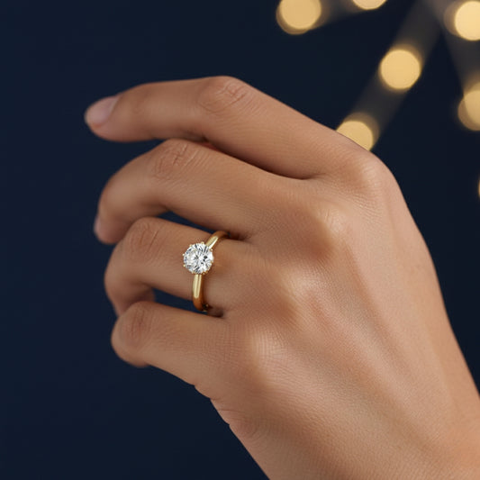 Hand wearing a gold ring with a 1ct moissanite diamond on a dark background with blurred lights