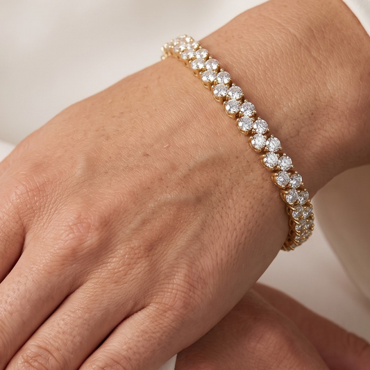A close-up of a gold tennis bracelet with clear round-cut moissanite gemstones worn on a person's wrist.