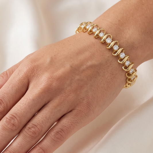 A close-up of a person's wrist wearing a gold tennis bracelet with small clear moissanite gemstones, set against a soft cream-colored background.