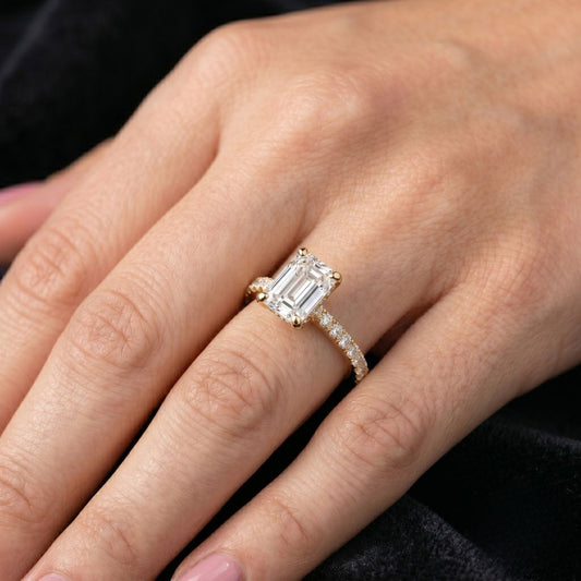 Close-up of a hand wearing a moissanite diamond ring with a black background
