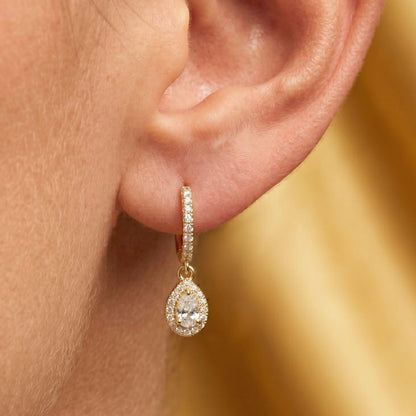 Gold earring with a clear Moissanite gemstone worn by an ear against a blurred gold background