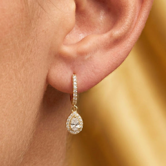Gold earring with a clear Moissanite gemstone worn by an ear against a blurred gold background