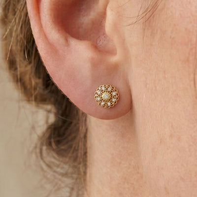 Close-up of a gold moissanite diamond earring worn on an ear with a neutral background