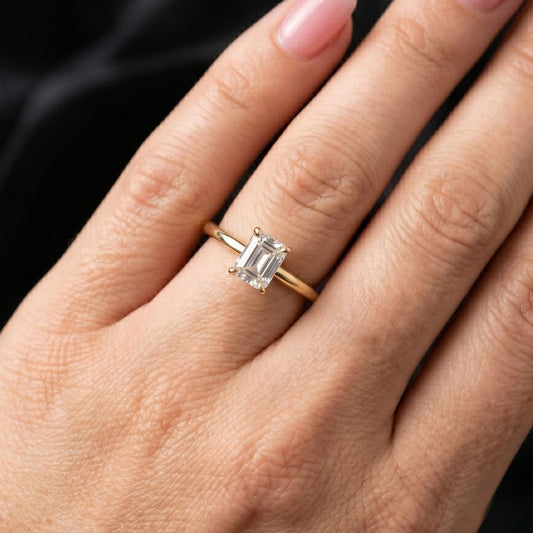 Gold ring with a moissanite diamond on a hand against a dark background