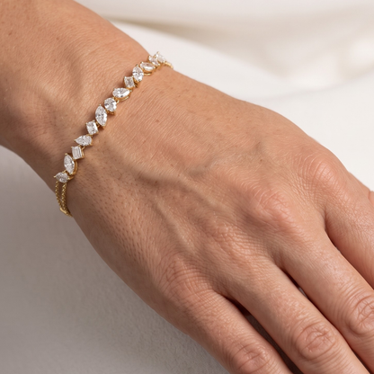A delicate yellow gold bracelet with marquise and baguette-cut clear moissanite stones, shown worn on a person's wrist against a soft white background.