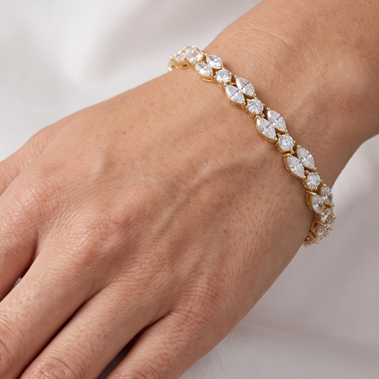 A close-up of a gold tennis bracelet with marquise-cut clear moissanite stones worn on a person's wrist.