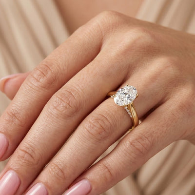 Gold ring with a moissanite diamond on a hand against a neutral background