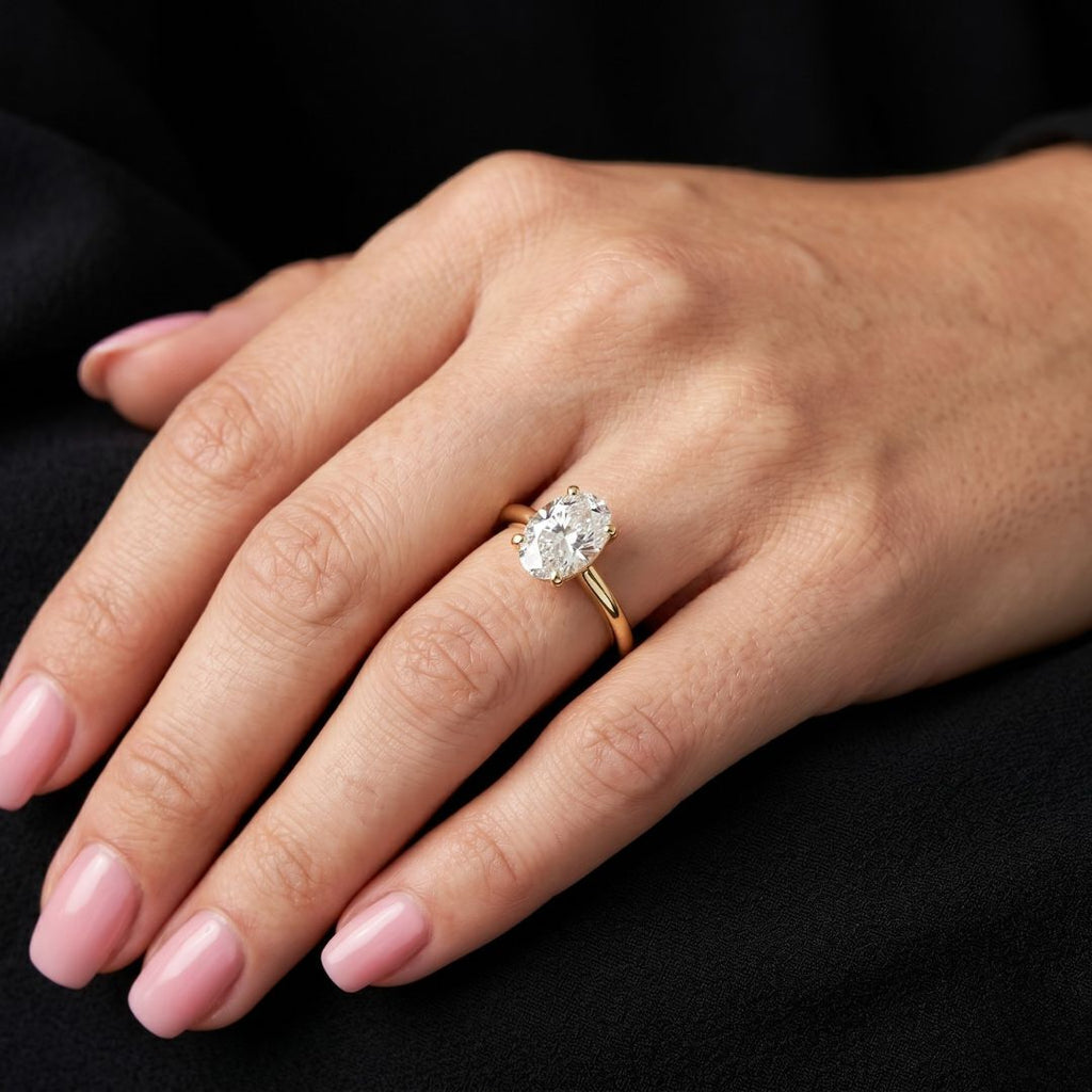 Hand wearing a gold ring with a moissanite diamond on a black background