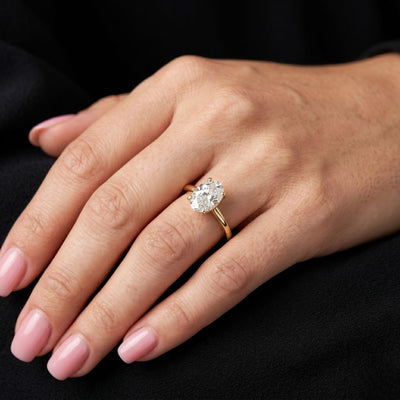 Hand wearing a gold ring with a moissanite diamond on a black background