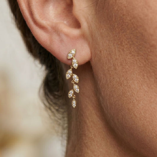 Gold earrings with clear Moissanite stones worn by a person, close-up on ear.