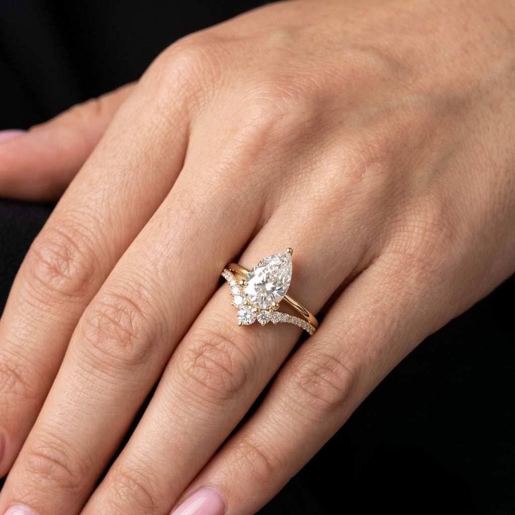 Gold ring with a pear-shaped moissanite diamond on a hand against a black background