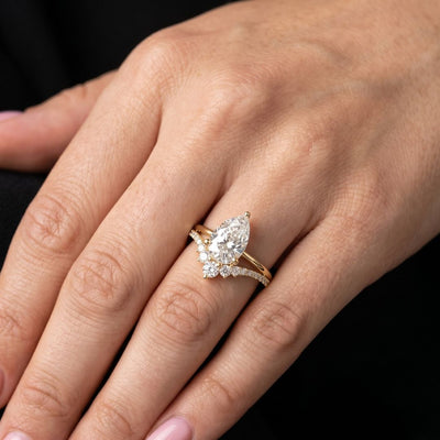 Gold ring with a pear-shaped moissanite diamond on a hand against a black background