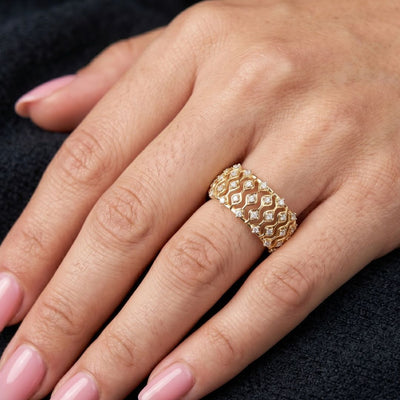 Gold ring with moissanite diamonds on a hand against a dark background