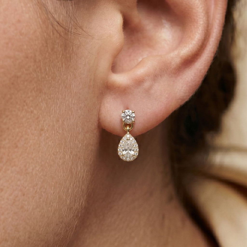 Close-up of a person wearing a gold teardrop earring with a moissanite diamond.
