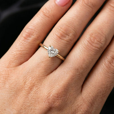 Rose gold ring with a moissanite diamond on a hand against a black background